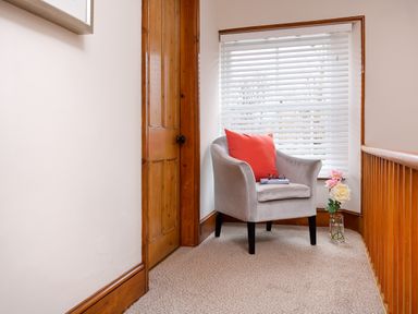 A gray armchair with a red pillow near a window with white blinds and a wooden door at Pippin Cottage in Keswick