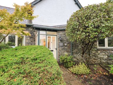 The entrance to a stone cottage with a white door and surrounding plants at Pudding Cottage in Ambleside