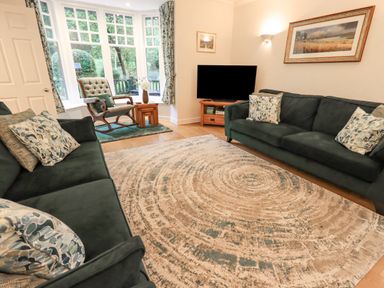 A living room with two sofas, a rocking chair by a bay window, a large rug, a television on a wooden stand, and framed artwork on the walls at Pudding Cottage in Ambleside