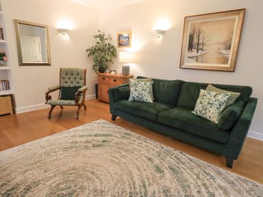 A living room with a green sofa and armchair a wooden cabinet and a landscape painting at Pudding Cottage in Ambleside