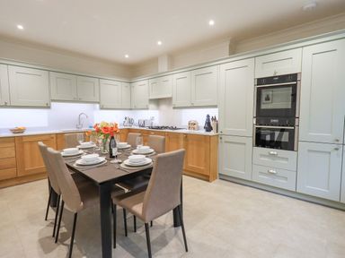 A kitchen with dining table set for six and cabinets along the walls at Pudding Cottage in Ambleside