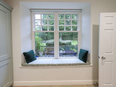 A window seat with cushions looking out to a garden with chairs and table at Pudding Cottage in Ambleside