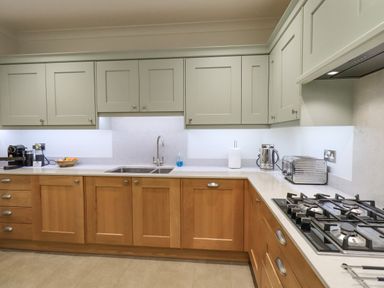 A kitchen with wooden lower cabinets grey upper cabinets gas stove toaster and sink at Pudding Cottage Ambleside