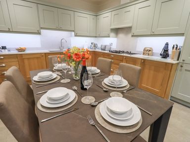 A kitchen with wooden and light-colored cabinets and a dining table set with plates glasses and cutlery at Pudding Cottage in Ambleside