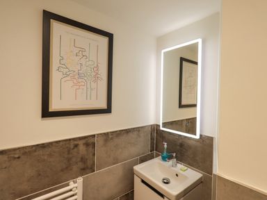 A bathroom with a sink a lit mirror a framed map on the wall and tiled lower walls at Pudding Cottage in Ambleside