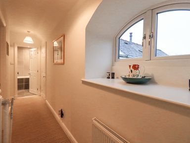 A hallway with a striped carpet and a half-open door leading to a bathroom with a bathtub at Pudding Cottage in Ambleside