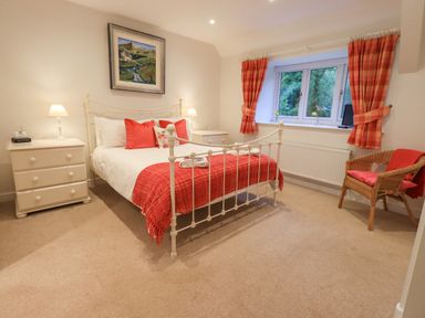 A bedroom with a bed a chair a window and two bedside tables at Pudding Cottage in Ambleside