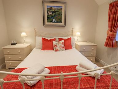 A bedroom with a bed with red and floral pillows bedside tables with lamps and folded towels on a red blanket at Pudding Cottage in Ambleside