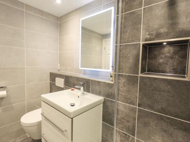 A bathroom with a toilet a sink a backlit mirror and tiled walls at Pudding Cottage in Ambleside