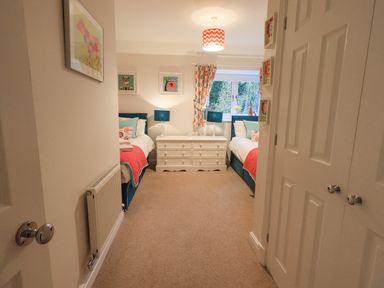 A bedroom with two beds a white dresser two blue lamps and patterned curtains at Pudding Cottage in Ambleside