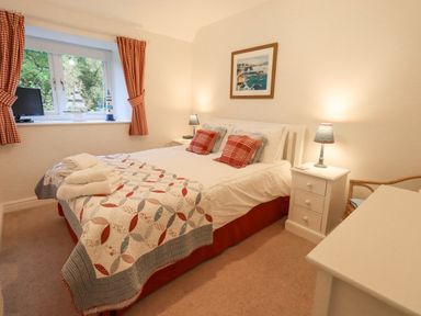 A bedroom with a double bed bedside tables lamps window with red check curtains and a dresser at Pudding Cottage in Ambleside