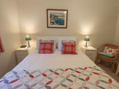 A bedroom with a bed two bedside tables with lamps a wicker chair and framed picture on the wall at Pudding Cottage Ambleside