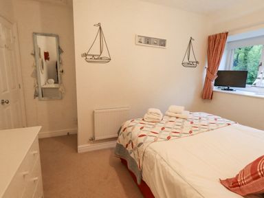 A bedroom with a bed, dresser, mirror, wall decorations, window, and television at Pudding Cottage in Ambleside