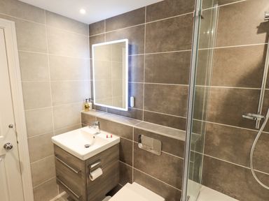 A bathroom with a sink, illuminated mirror, shower enclosure, and a toilet at Pudding Cottage in Ambleside