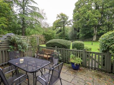 An outdoor patio with a metal table and chairs a wooden bench and plants at Pudding Cottage in Ambleside