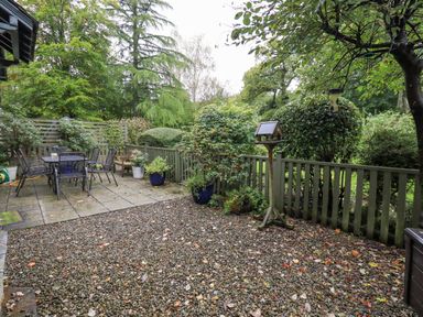 An outdoor patio area with a table and chairs surrounded by plants and a wooden fence at Pudding Cottage in Ambleside