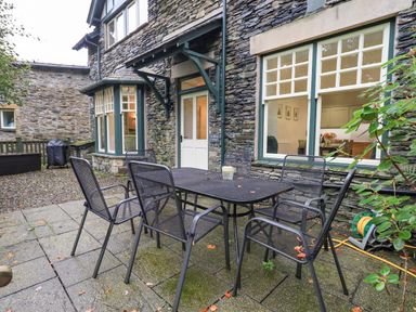 An outdoor patio area with a black metal table and six matching chairs at Pudding Cottage in Ambleside