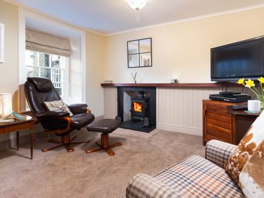 A living room with a leather chair and footstool a fireplace and a television at Ghyll Foot Cottage in Ambleside