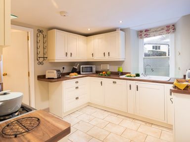 A kitchen with white cabinets a microwave a toaster a sink and vegetables on the counter at Ghyll Foot Cottage Ambleside