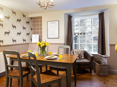 A dining room with a wooden table set for four and a leather armchair by a window at Ghyll Foot Cottage Ambleside