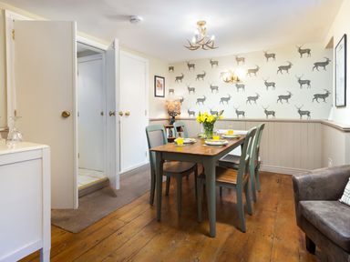 A dining room with a wooden table and four chairs set with plates and glasses with daffodils in a vase on the table and deer wallpaper at Ghyll Foot Cottage in Ambleside
