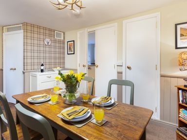 A dining room with a wooden table set for four with yellow napkins and drinks at Ghyll Foot Cottage in Ambleside