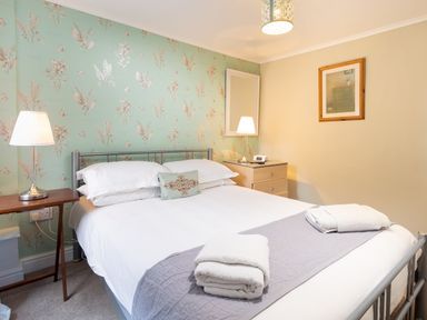 A bedroom with a double bed two bedside tables lamps and folded towels on the bed at Ghyll Foot Cottage in Ambleside