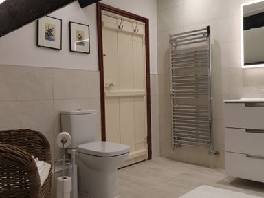 A bathroom with a toilet a wicker basket a towel rack a mirror and a door at Ghyll Foot Cottage in Ambleside