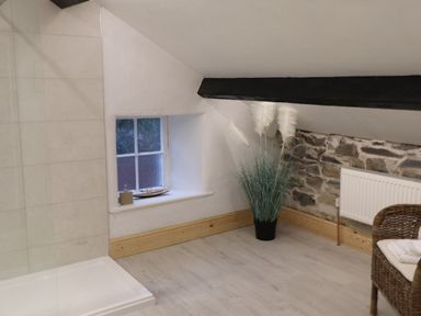 A bathroom with a small window and shower area with a stone wall and a wicker chair at Ghyll Foot Cottage in Ambleside