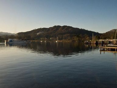 A lake with a boat on the water and hills in the background at Ghyll Foot Cottage in Ambleside
