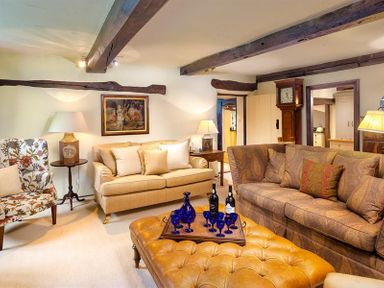 A living room with a beige sofa floral armchair a brown patterned sofa and a tufted ottoman at Fair Rigg Old Farm in Cartmel