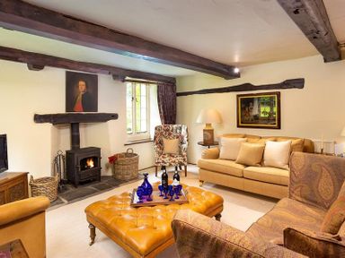 A living room with a fireplace two sofas an armchair and a large ottoman with a tray of bottles and glasses at Fair Rigg Old Farm in Cartmel