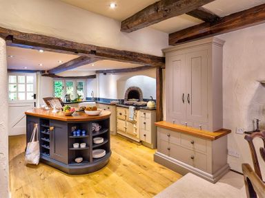 A kitchen with wooden beams a kitchen island and a cabinet at Fair Rigg Old Farm in Cartmel