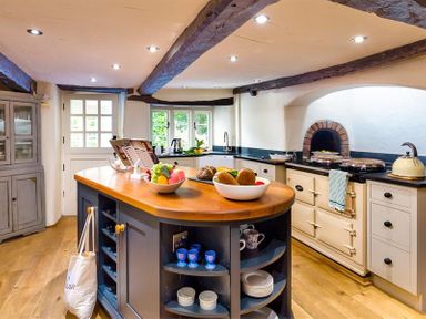 A kitchen with a wooden island with fruit bowls and shelves with cups and plates at Fair Rigg Old Farm in Cartmel