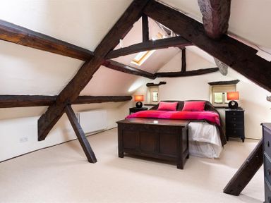 A bedroom with exposed wooden beams a bed with pink blankets and bedside tables with lamps at Fair Rigg Old Farm in Cartmel