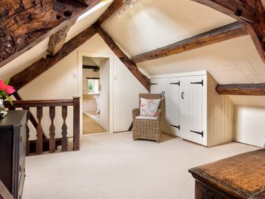 An attic room with exposed wooden beams a wicker chair a wooden banister and white storage cupboards at Fair Rigg Old Farm in Cartmel