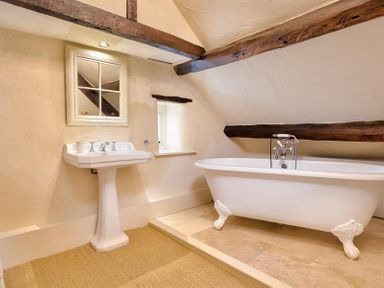 A bathroom with a pedestal sink and a clawfoot bathtub under exposed wooden beams at Fair Rigg Old Farm in Cartmel