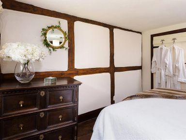 A bedroom with a wooden dresser vase of flowers round mirror white robes hanging on the wall at Fair Rigg Old Farm in Cartmel