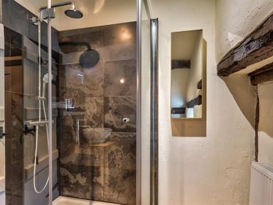 A bathroom with a glass shower enclosure dark wall tiles and a rectangular mirror on a textured wall at Fair Rigg Old Farm in Cartmel