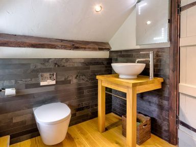 A bathroom with a white toilet a wooden sink table a round white basin and a mirror at Fair Rigg Old Farm in Cartmel