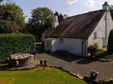 A white cottage with a sloped roof and outdoor seating area on a gravel patio at Fair Rigg Old Farm in Cartmel