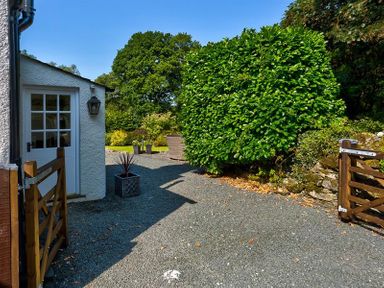 An outdoor area with a wooden gate a white door potted plants a gravel path and green bushes at Fair Rigg Old Farm in Cartmel
