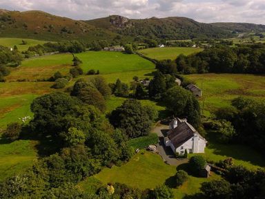 A countryside view with a white house surrounded by trees and green fields at Fair Rigg Old Farm in Cartmel