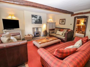 A living room with three sofas a wood burning stove a television and wall art at Low Cartmell Fold in Crosthwaite