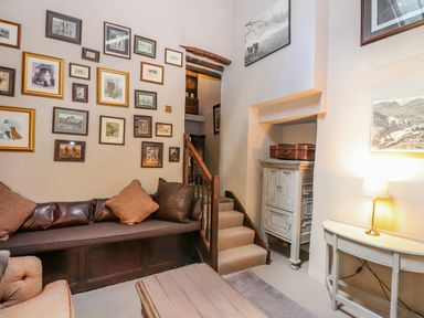 A living room with framed pictures on the wall a sofa stairs a small cabinet and a table with a lamp at Low Cartmell Fold in Crosthwaite