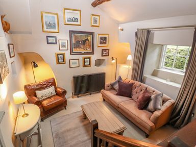 A living room with a leather armchair a sofa a wooden coffee table framed pictures on the wall and a window at Low Cartmell Fold in Crosthwaite