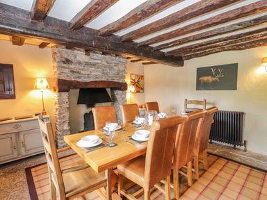 A dining room with a wooden table set for six in front of a stone fireplace at Low Cartmell Fold in Crosthwaite