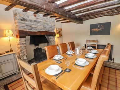 A dining room with a wooden table set for six and a stone fireplace at Low Cartmell Fold in Crosthwaite