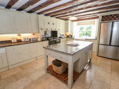 A kitchen with an island countertop a stainless steel refrigerator wooden ceiling beams and a window at Low Cartmell Fold in Crosthwaite