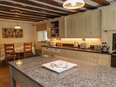 A kitchen with granite countertop island wooden chairs around a table with a lemon patterned tablecloth and cabinets with plates at Low Cartmell Fold in Crosthwaite